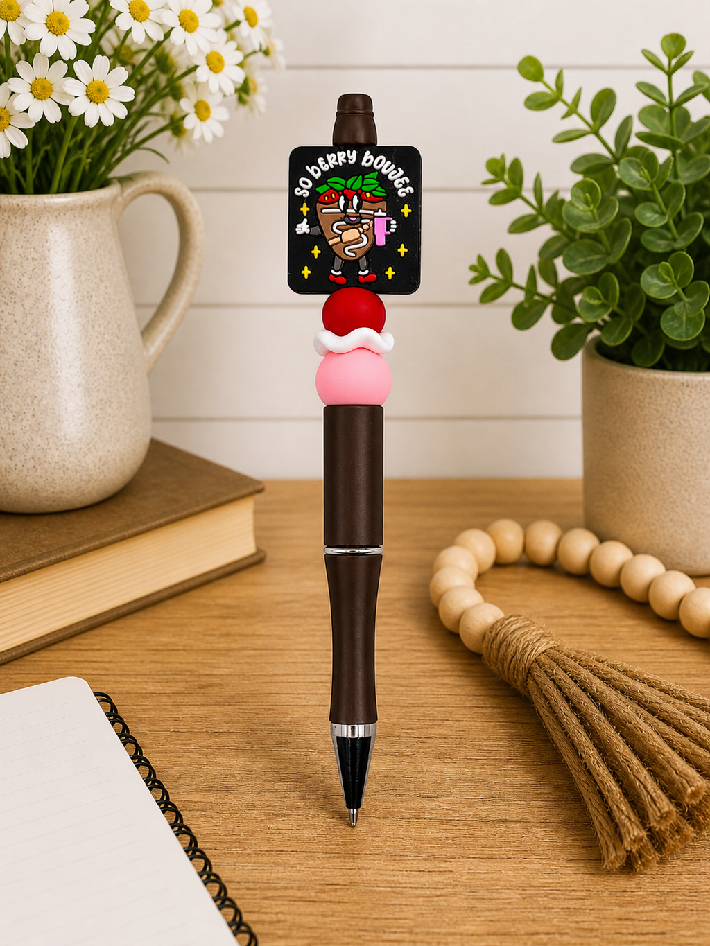 Novelty ballpoint pen with brown barrel, pink charm, and black logo topper.