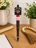 Novelty ballpoint pen with brown barrel, pink charm, and black logo topper.