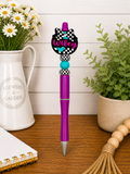 Purple ballpoint pen with checkered bow topper and teal bead accents
