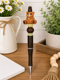 Black bear pen with teddy bear charm and green bead ring near tip.