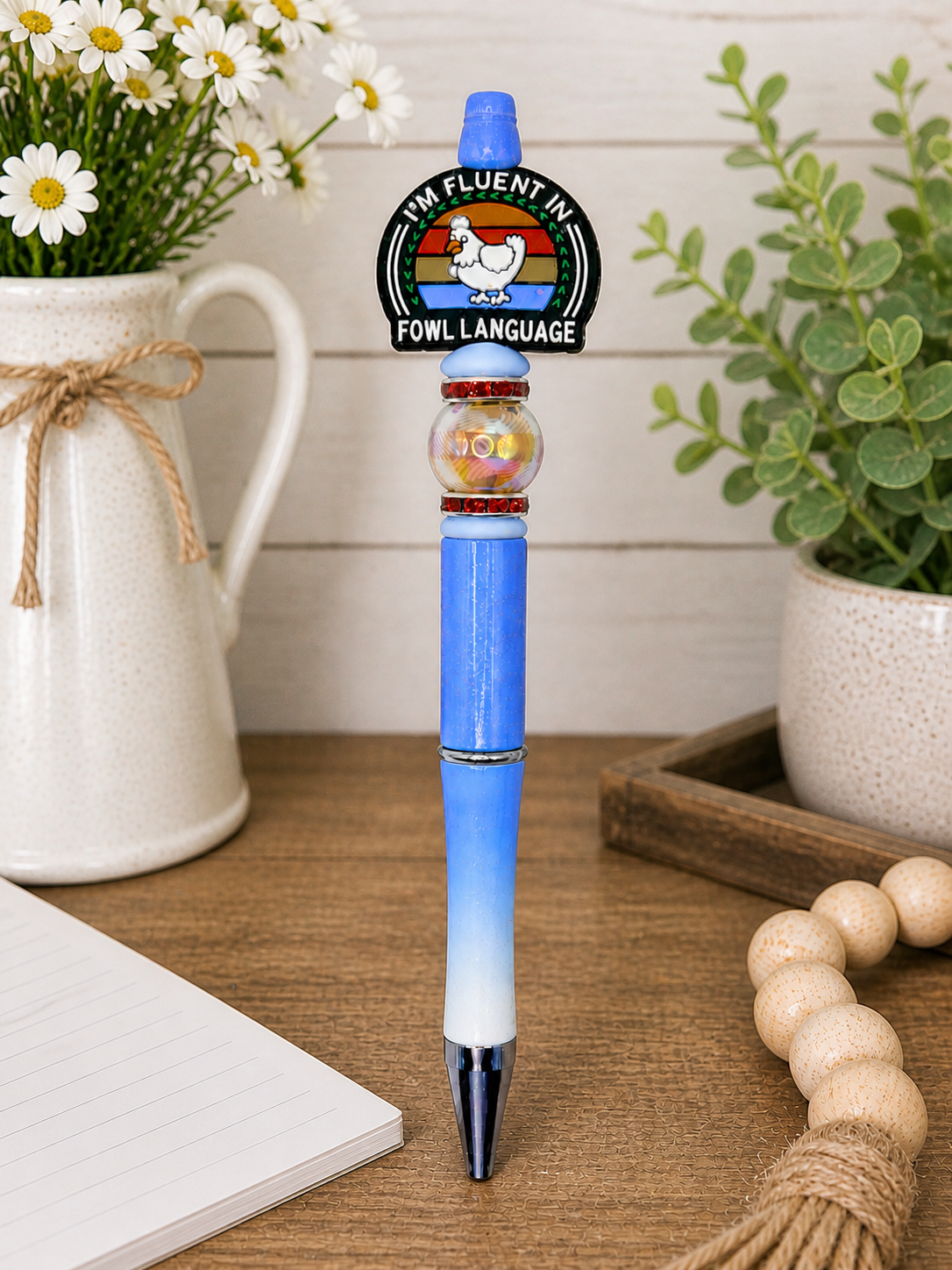Blue ballpoint pen with circular Fowl Language logo and clear glitter barrel