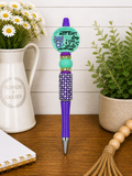 Purple beaded ballpoint pen with teal badge cap and sparkling purple bead grip