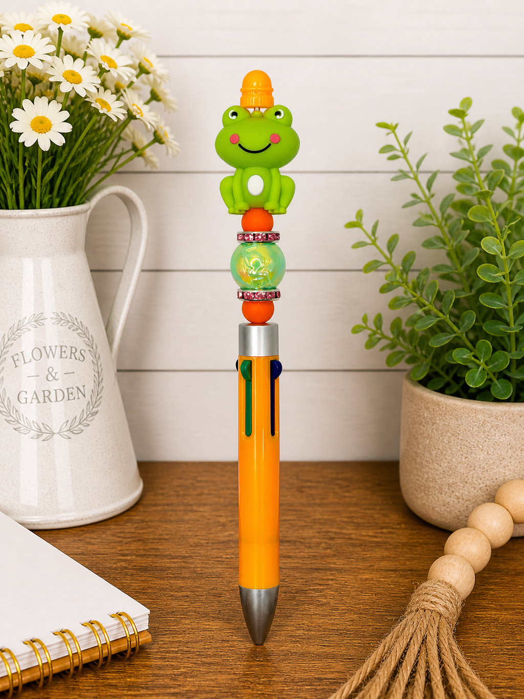 Orange ballpoint pen with smiling green frog topper and blue clip