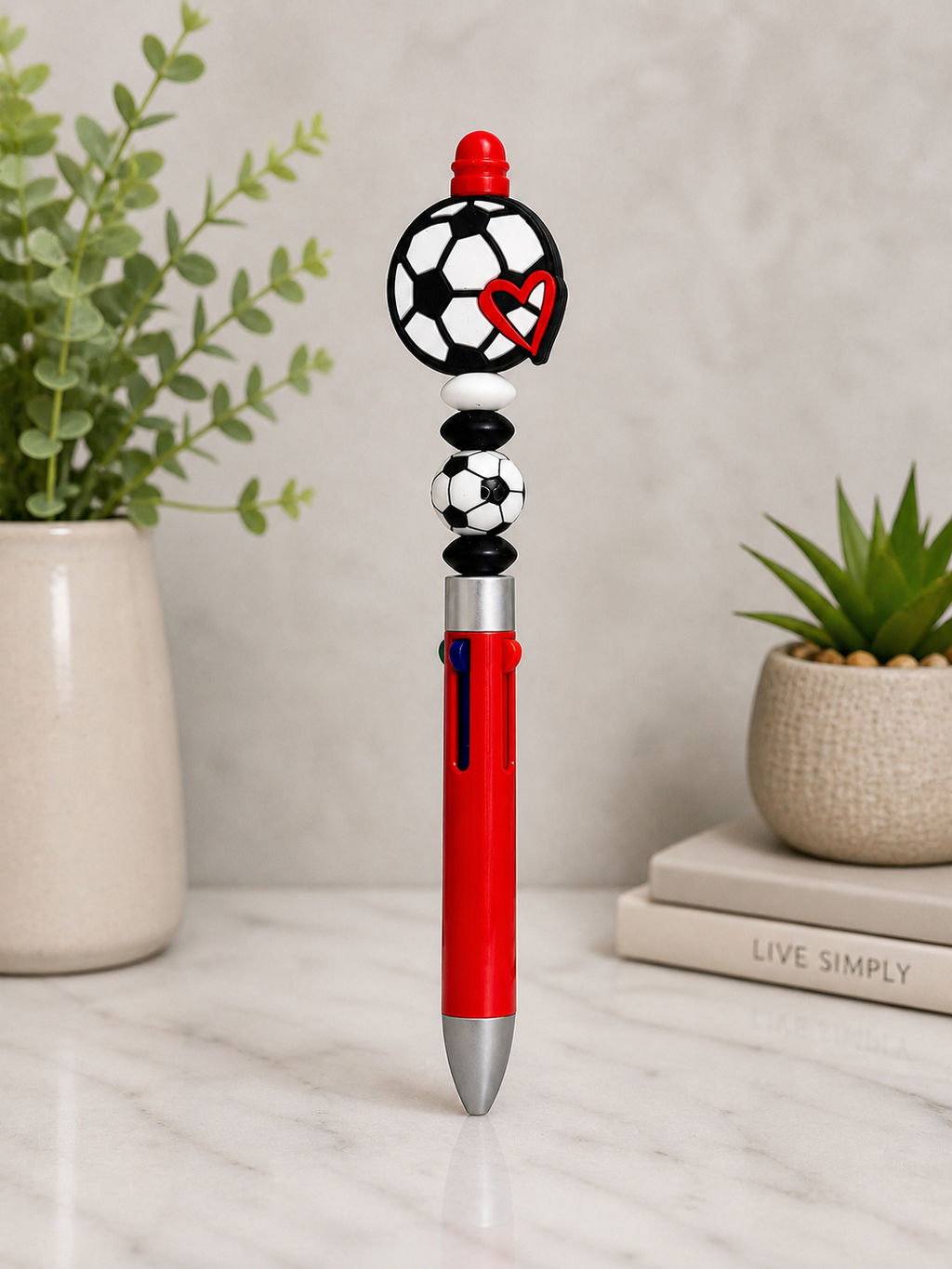 Soccer pen with red body, black soccer-ball topper and red heart detail, silver tip.