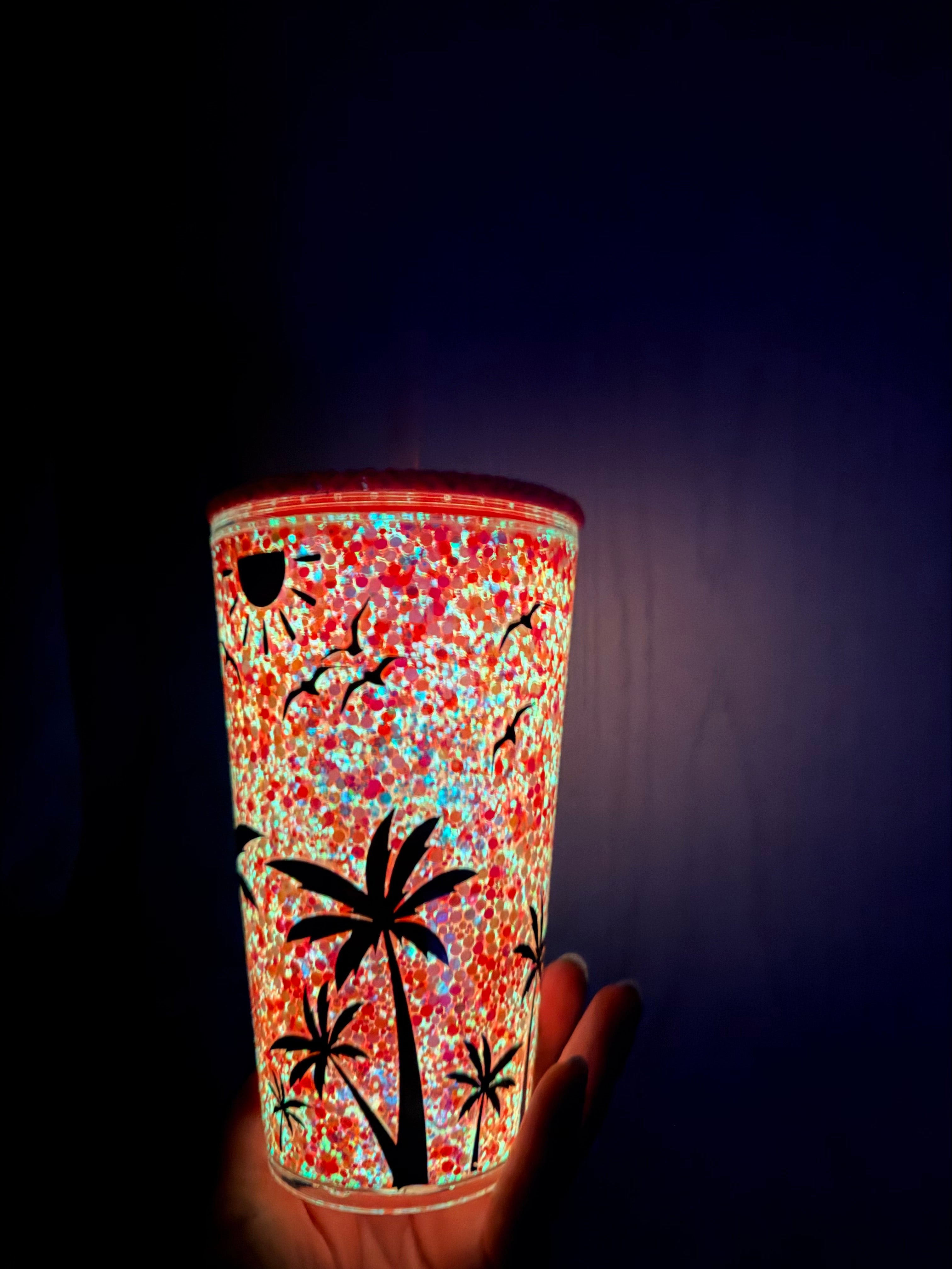 Glitter acrylic snow globe tumbler with illuminated gold-red sparkle and palm trees