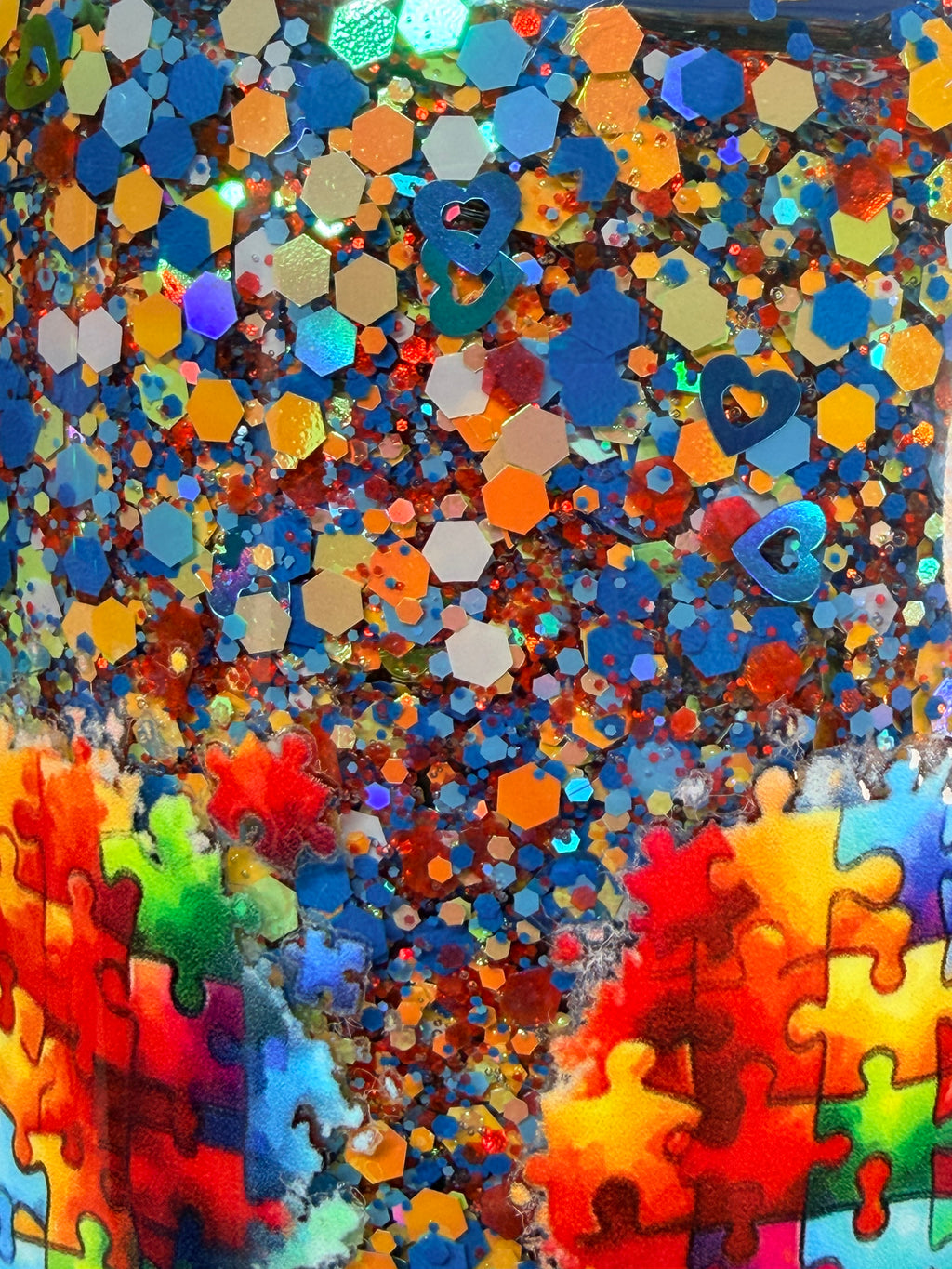 Close-up of colorful glitter and jigsaw-shaped pieces inside acrylic snow globe tumbler