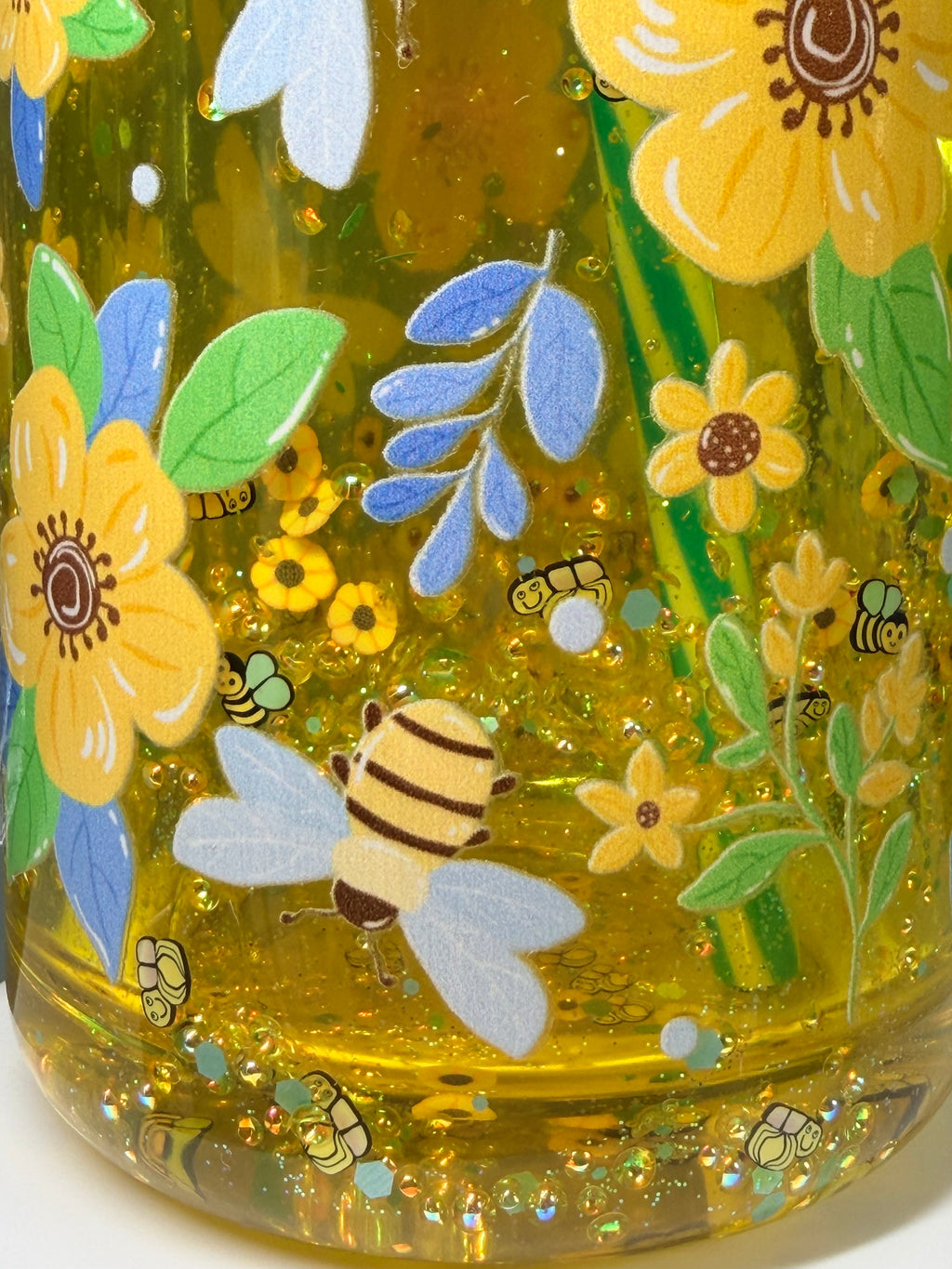 Close-up of green mug bottom print with bees, flowers, and gold glitter speckles