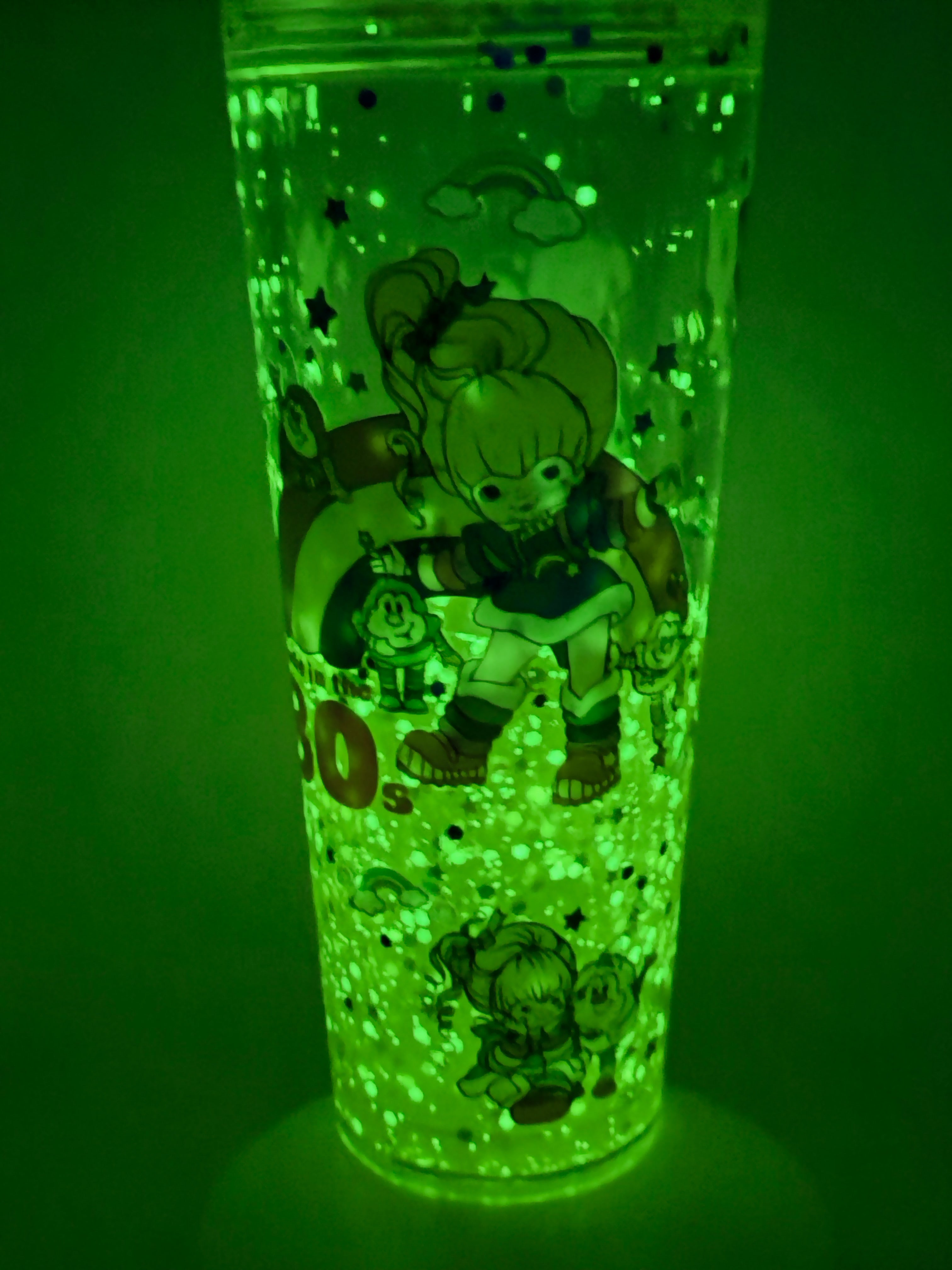 Lava snow globe cup glowing green with character silhouettes, glitter bubbles, straw